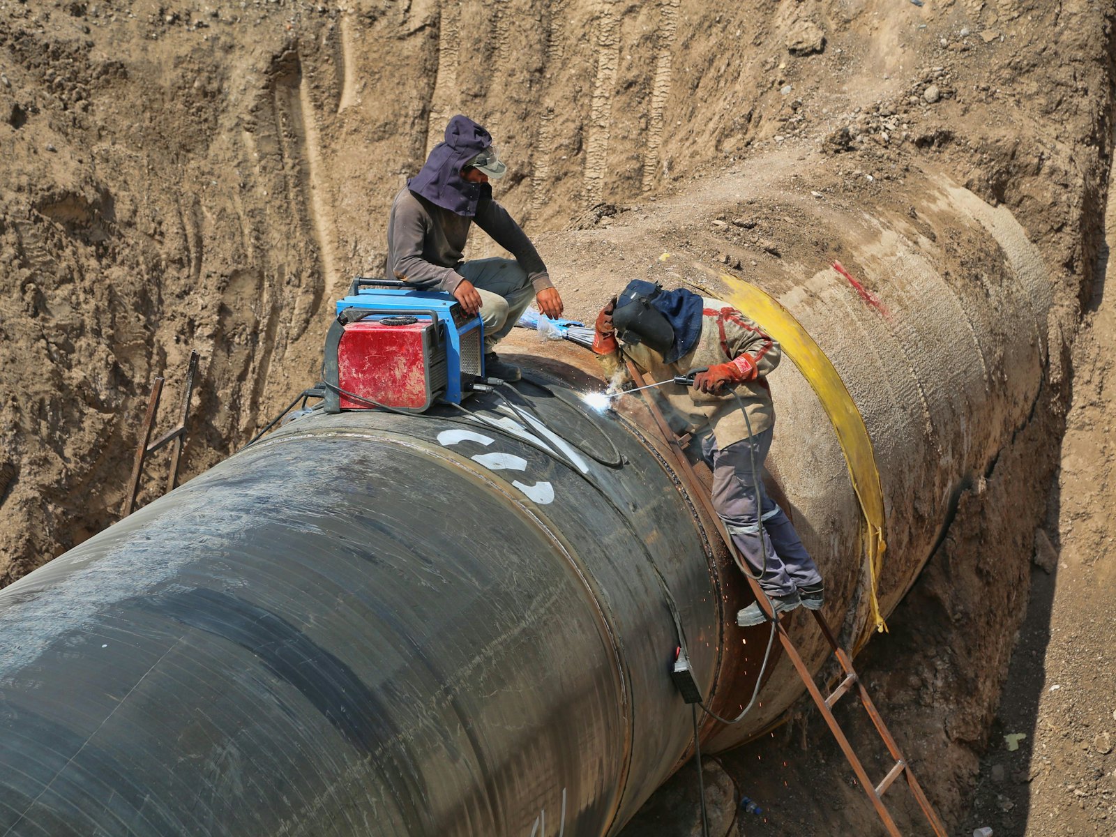 Welders working on a large-diameter pipeline in an open trench