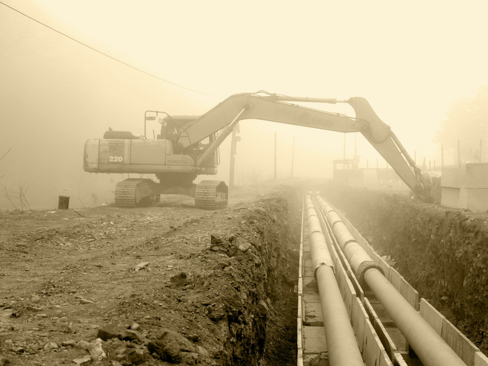 Excavator working beside a pipeline string in dusty conditions